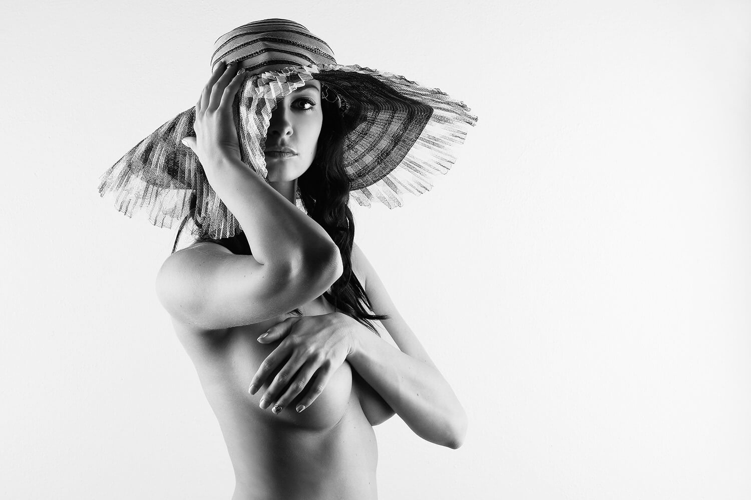 černobílá boudoir fotografie ženy s kloboukem na světlém pozadí