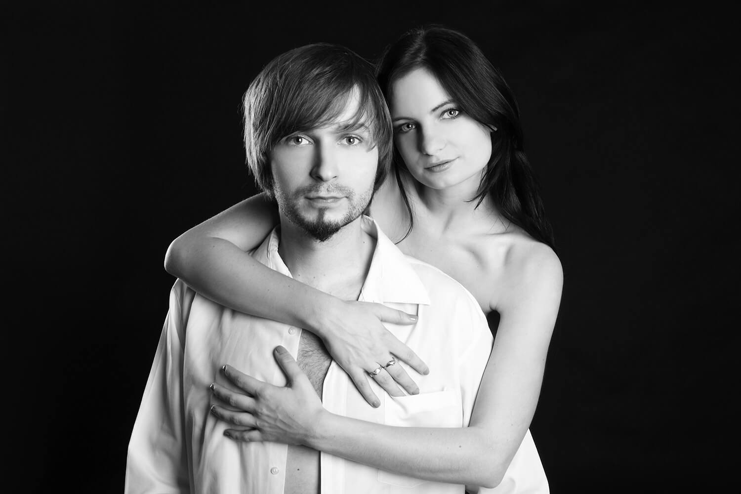 black and white couple photo of a woman embracing a man in a shirt on a dark background
