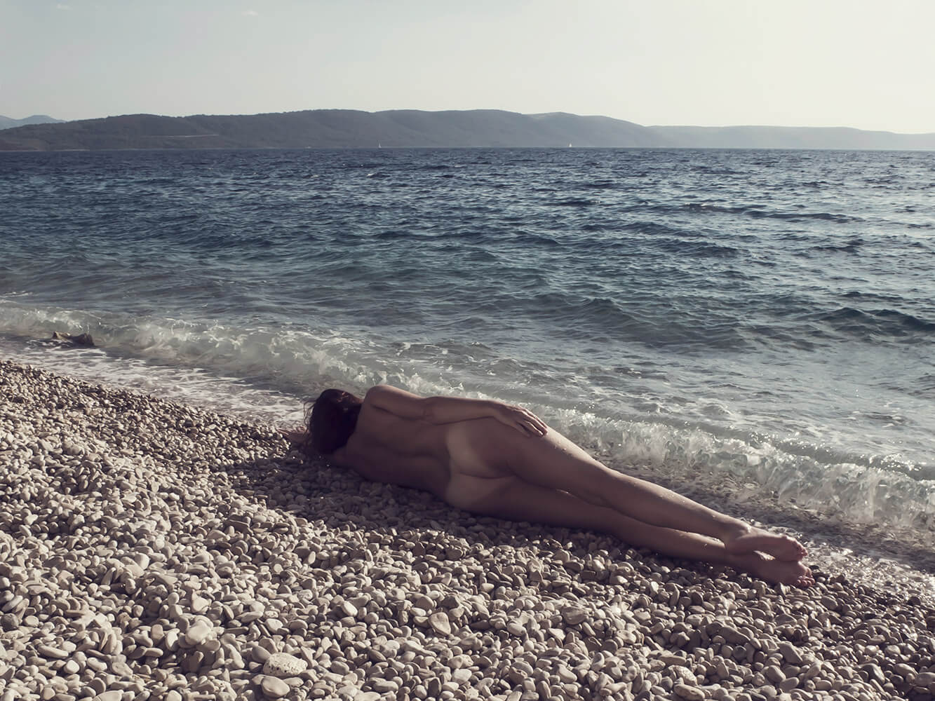 ležící ženský umělecký akt na oblázkové pláži u moře