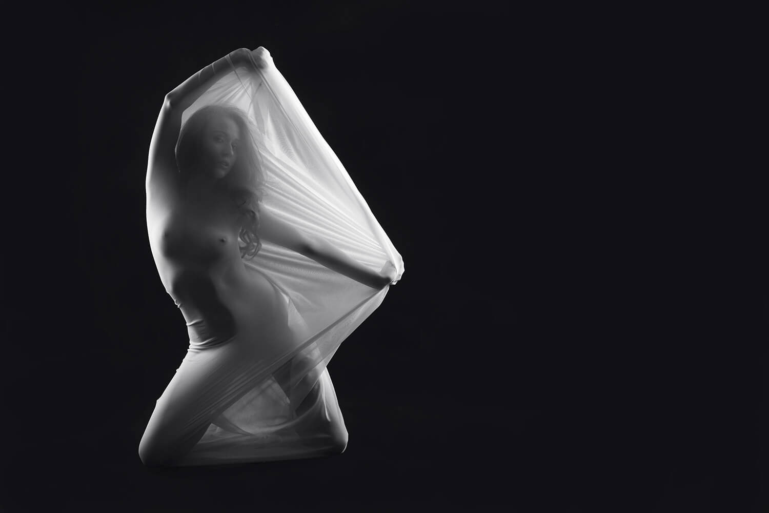 black and white fine art nude of a woman with light fabric on a dark background