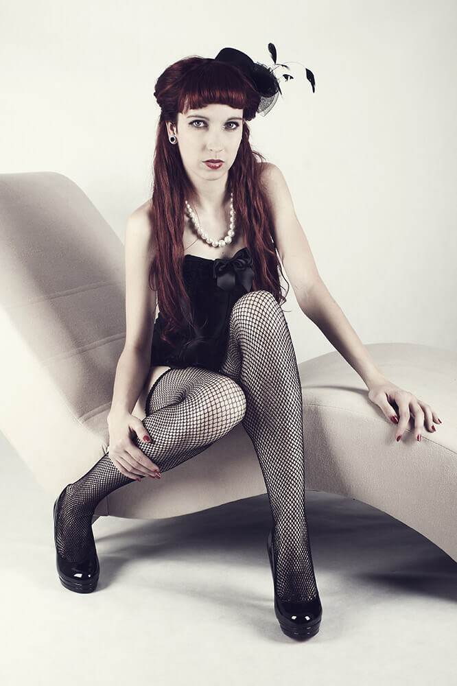boudoir photo of a woman in a black corset and fishnet stockings on a sofa
