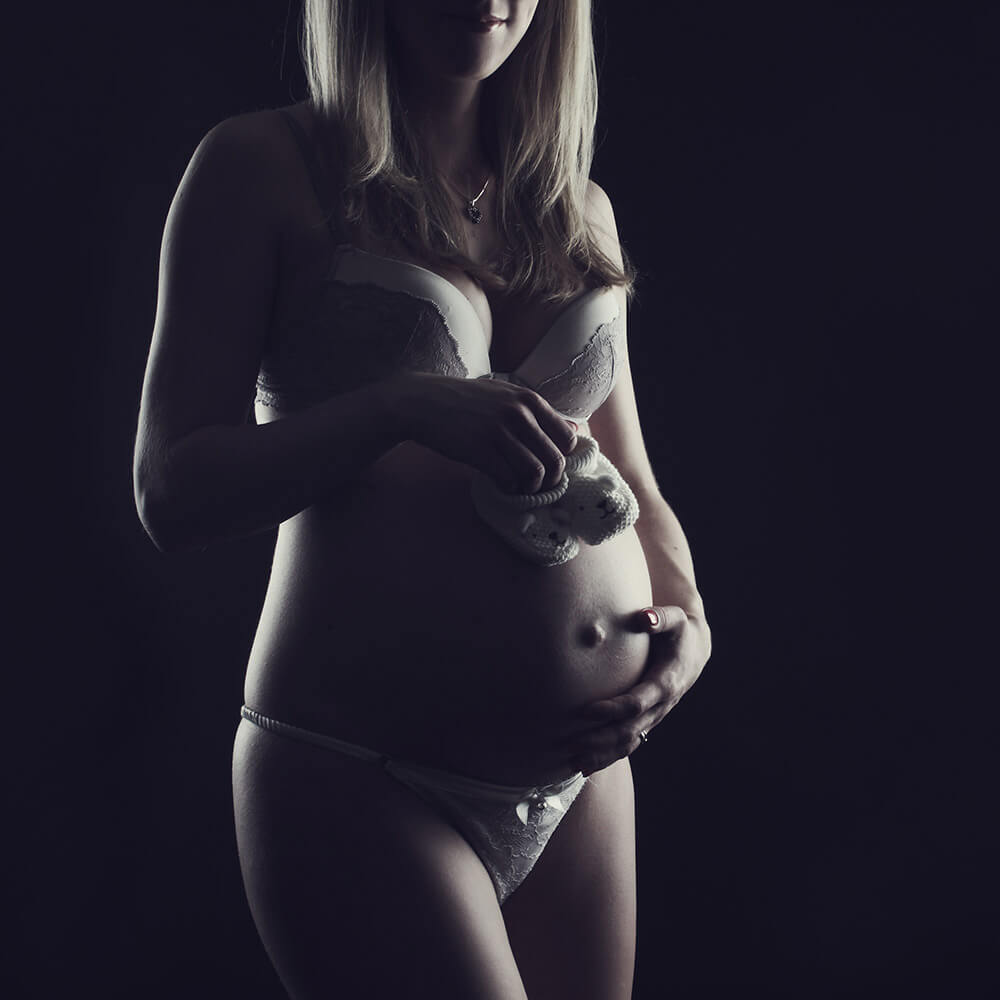 těhotenská fotografie v prádle a s botičkami na tmavém pozadí laděná do hněda