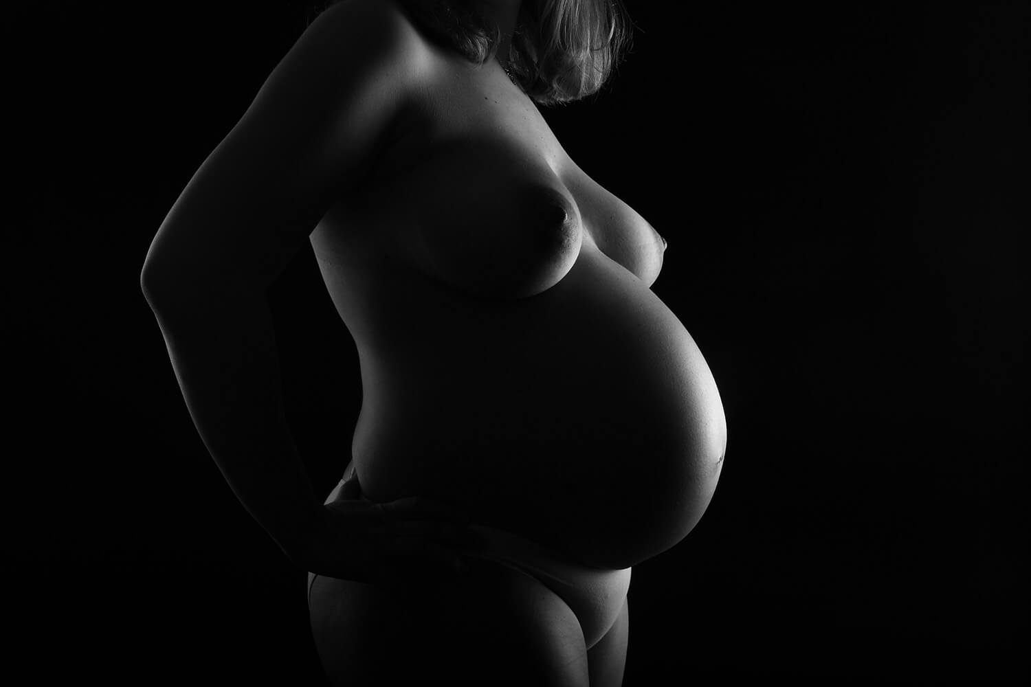 černobílá těhotenská silueta na tmavém pozadí