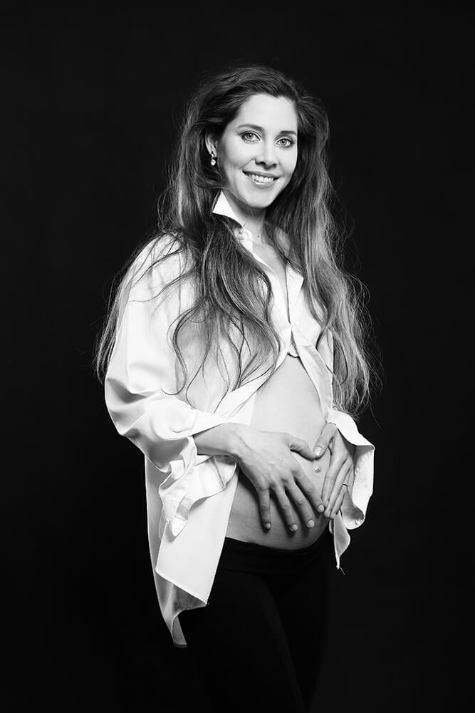 černobílá těhotenská fotografie ve světlé košili na tmavém pozadí