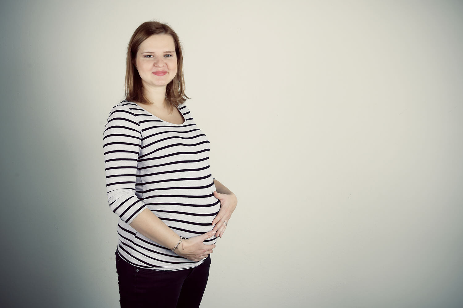 těhotenská fotografie v pruhovaném triku a černých kalhotách na světlém pozadí