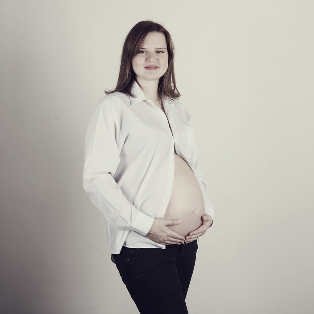 těhotenská fotografie v bílé košili a černých kalhotách na světlém pozadí