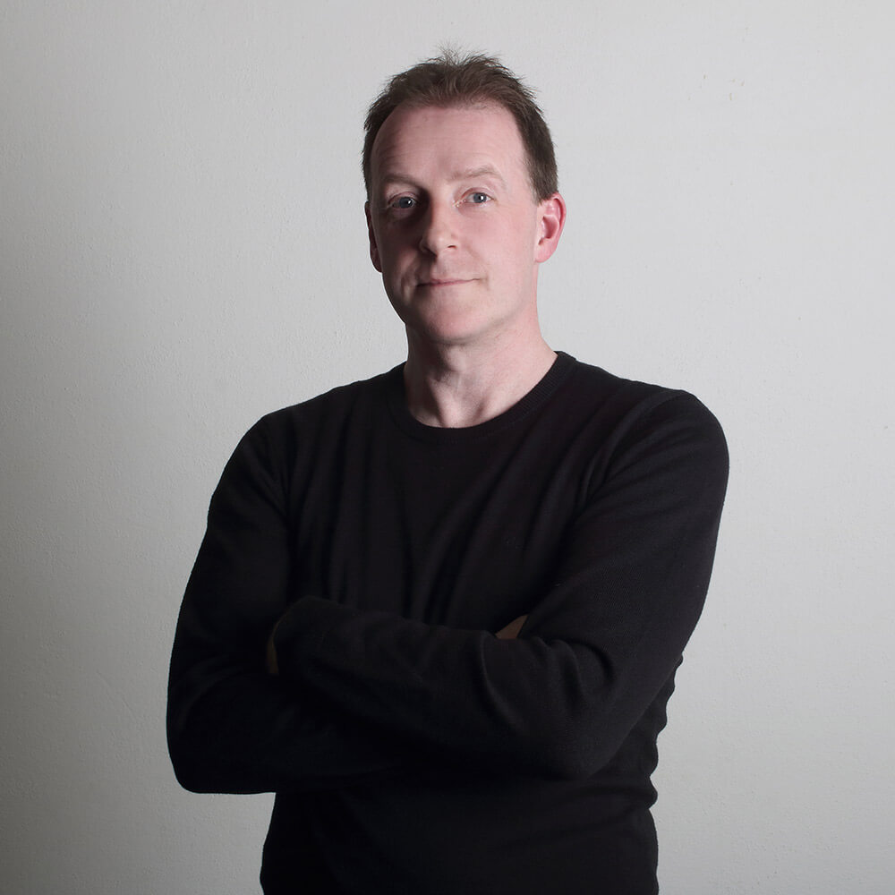 male portrait in a black T-shirt with folded arms on a light background