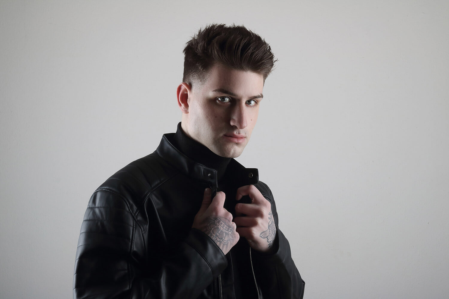 male portrait in a black turtleneck with a leather jacket and with a tattoo, on a light background