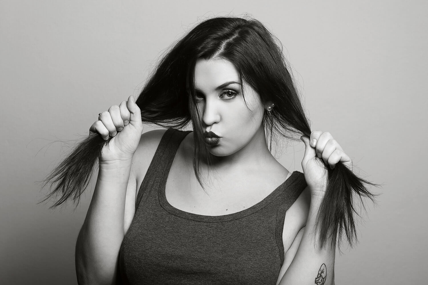 black and white female portrait in a dark tank top and with her hands holding her hair on a light background