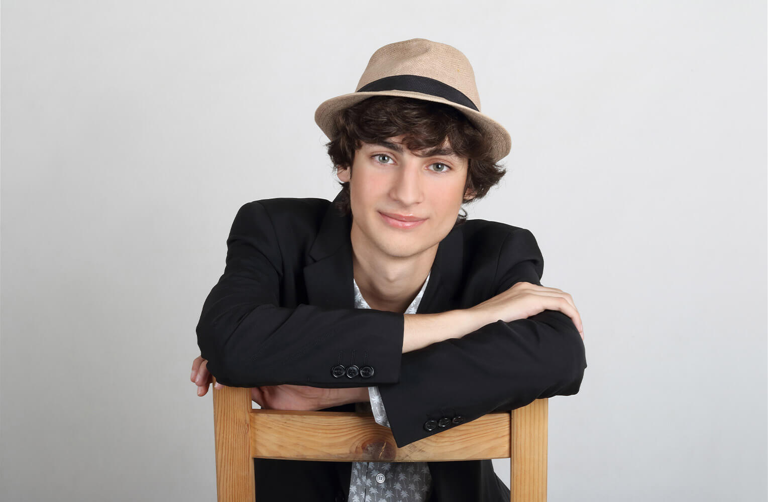 sedící umělecký portrét mladého herce s kloboukem na hlavě na světlém pozadí
