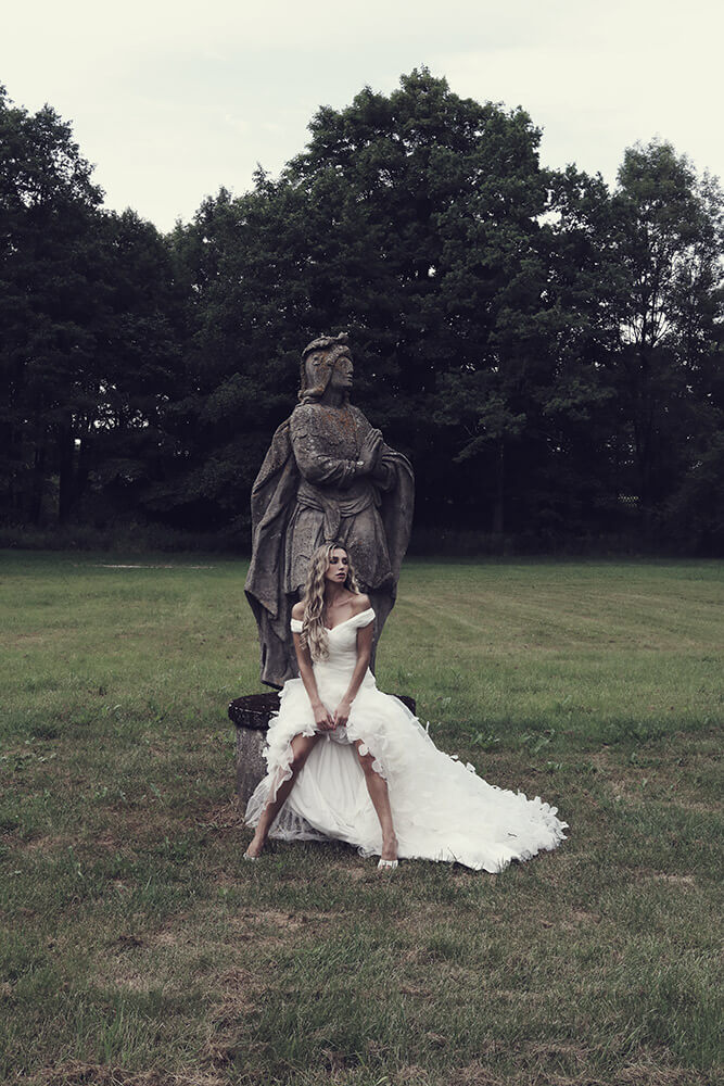 Nevěsta ve svatebních šatech focená v přírodě u sochy.