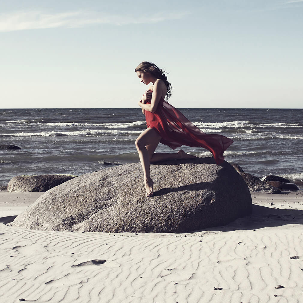 fotografie ženy klečící na jednom koleni na velkém kameni na břehu moře