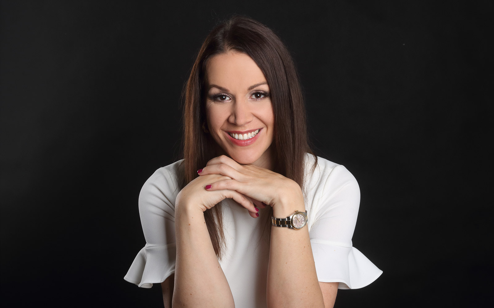 Studio business portrait of a smiling woman in a white top against a dark background.
