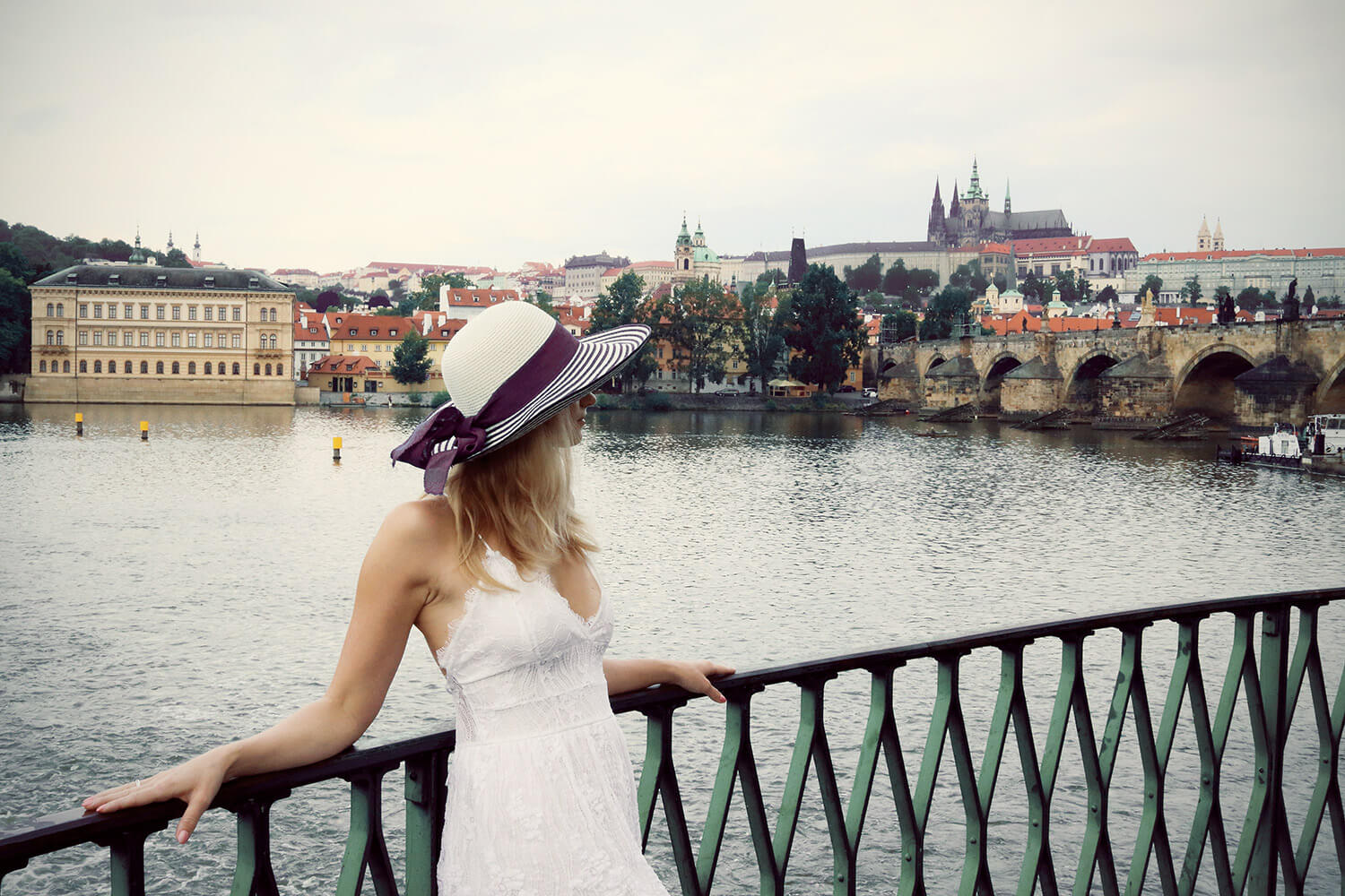 lifestyle fotografie ženy v bílých šatech a klobouku s Karlovým mostem a Pražským hradem v pozadí